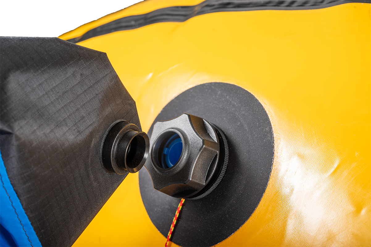 Close-up of a Flextail Pump / Inflation Bag Adapter by Alpacka on a yellow inflatable, showing a black cap with surrounding black and blue material, compatible with TAV adapters for use with mini inflator pumps.