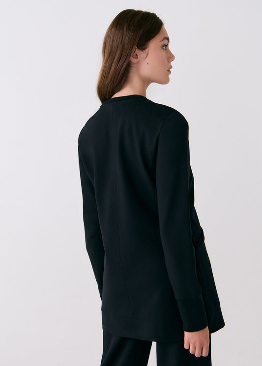 A woman with long brown hair wears the Lole Mindset Tunic, standing facing away and slightly to the side against a plain light background.