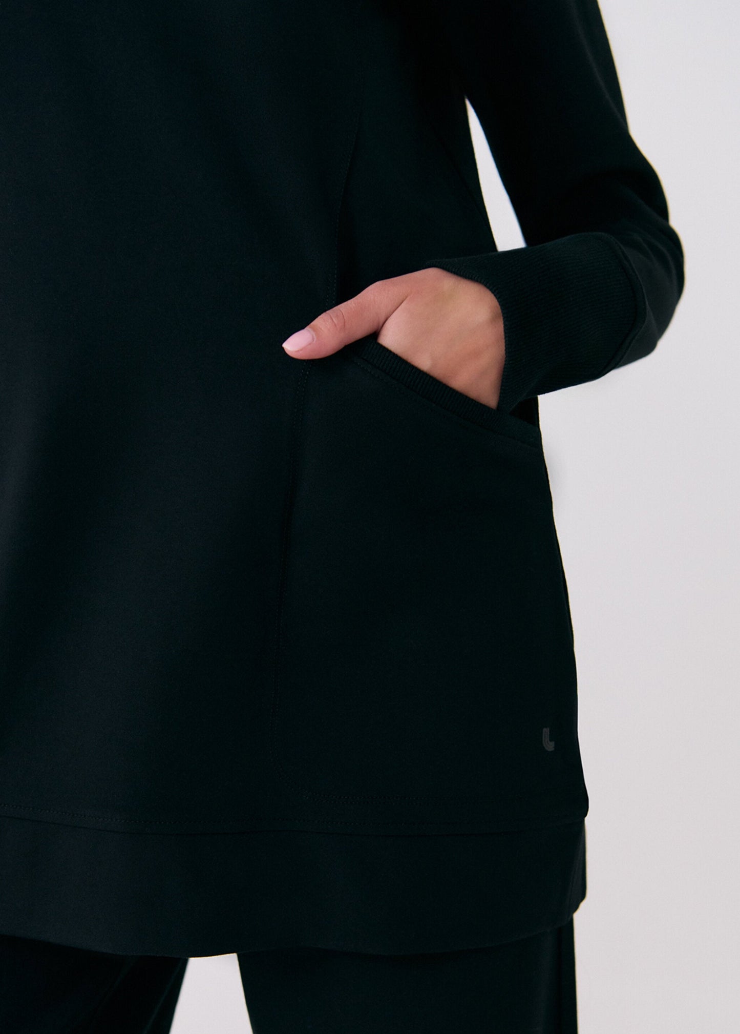 A person wearing the Lole Mindset Tunic, a classic fit, long-sleeved black top, and black pants with their right hand partially inside a side pocket.