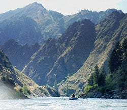 a man in a boat on a river with mountains in the background.