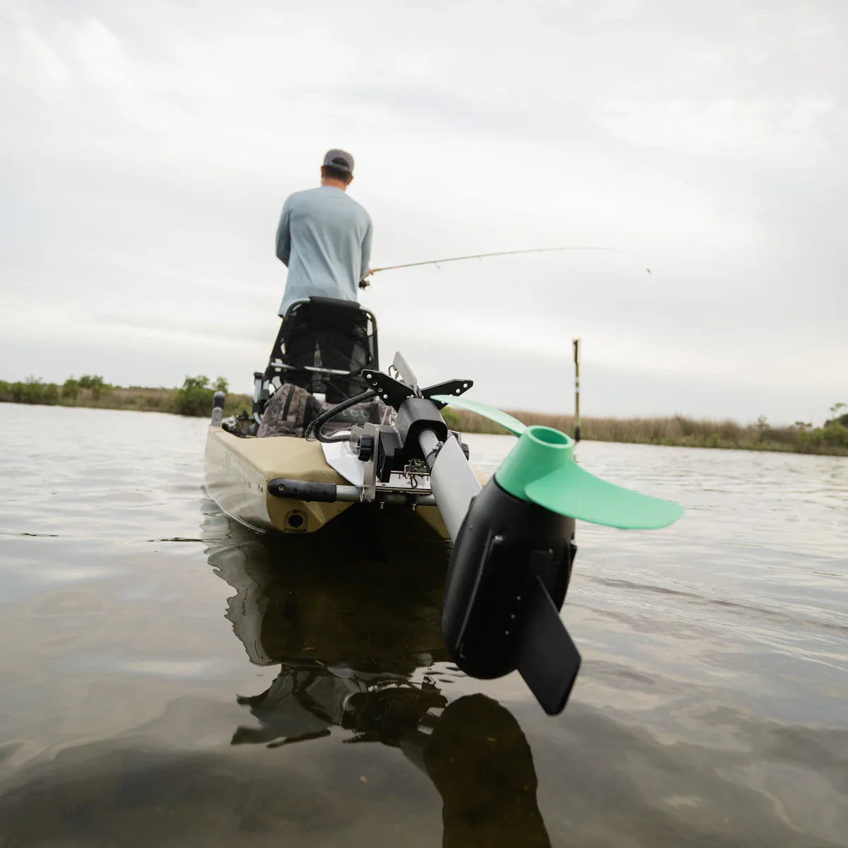 A person glides effortlessly across calm waters from a kayak equipped with Newport's NK300 Motor + 36V50 LoPRO Battery Bundle, under a cloudy sky.