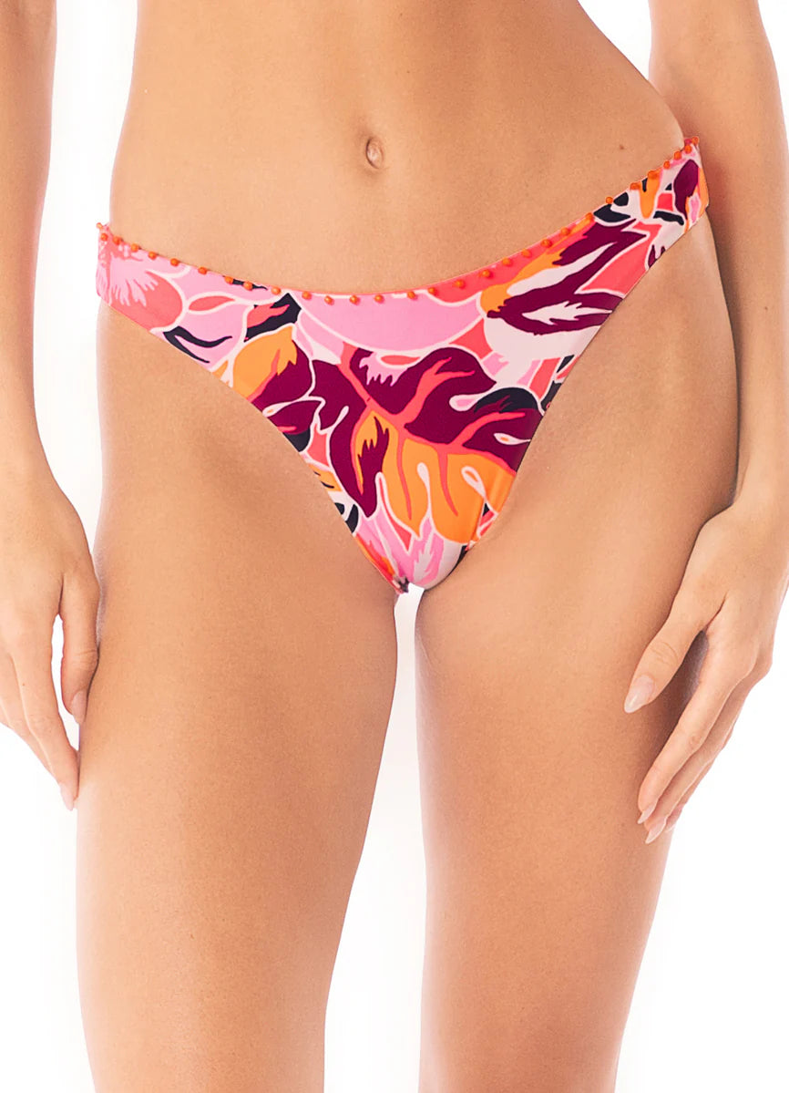 Someone models the Maaji Sublimity Bikini bottom—a colorful, reversible low-rise piece with pink, orange, red, and purple floral patterns. This swimwear also features UPF 50 protection and is shown from mid-torso to upper thighs.