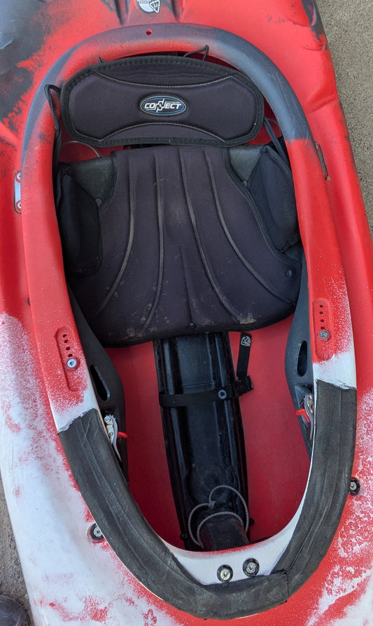Top-down view of a Used Pyranha Machno SM kayak seat in red and black from 4Corners Riversports, with visible footrests and light wear around the cockpit rim—suitable for all skill levels.