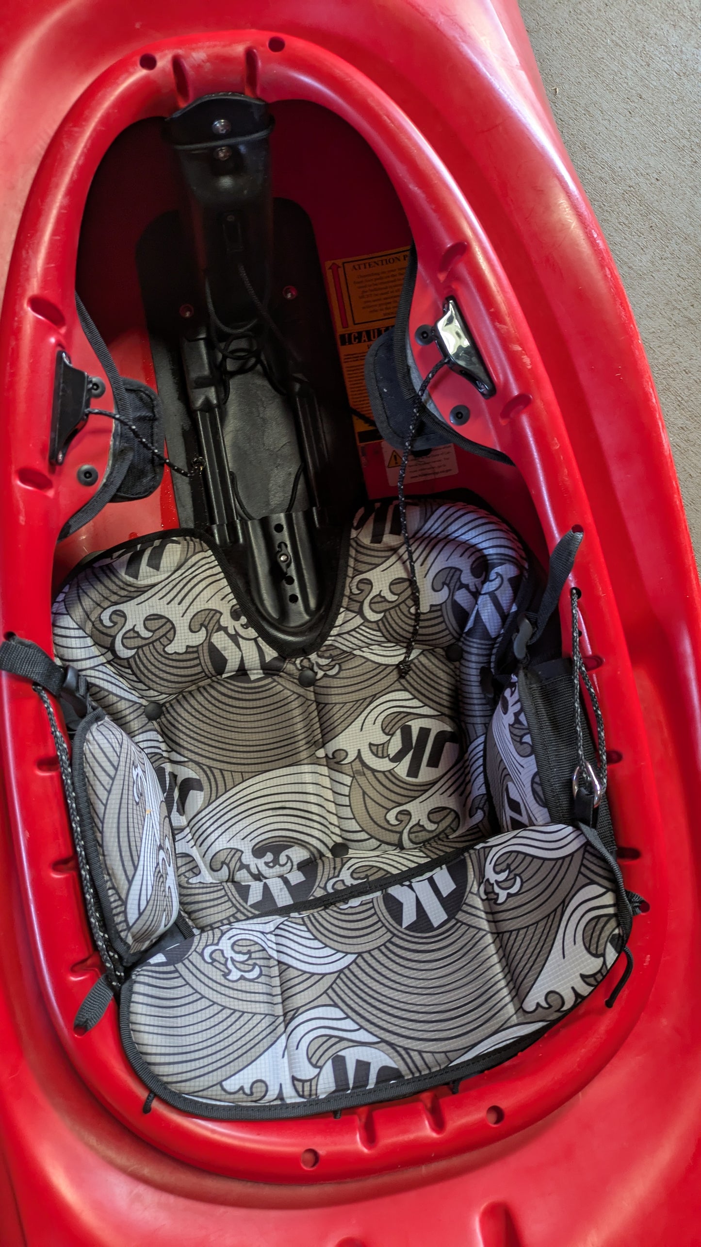 Close-up of the cockpit in a red Jackson Kayak Demo Flow SM, featuring a black and white patterned cushioned seat with straps and footrests.