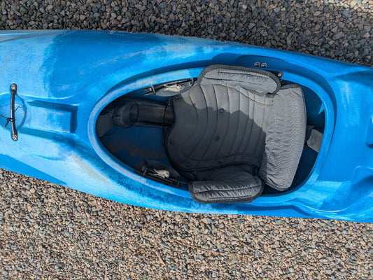 Top view of a Consignment LiquidLogic Remix 69 kayak by LiquidLogic, featuring a gray padded seat, shown resting on small, round gravel stones.