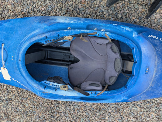 A Consignment Wavesport ZG by Wavesport, a blue freestyle kayak with open cockpit and padded seat, is pictured resting on gravel.