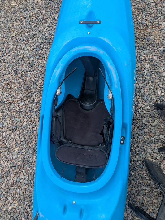 The Consignment Titan Rival by Titan Kayaks, in blue, rests on gravel, featuring a modern design with an open cockpit, black seat, and protective padding inside.