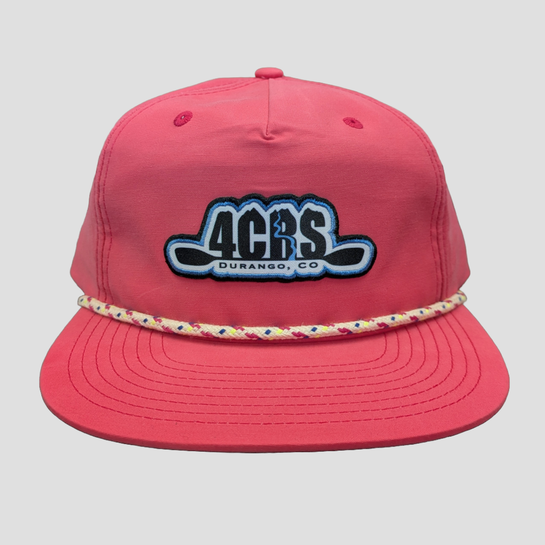 The 4CRS Pops Hat from 4Corners Riversports is a pink baseball cap with "4CRS Durango, CO" embroidered in black and blue. It features a colorful rope detail above the brim, making it perfect for sun-filled paddling adventures.