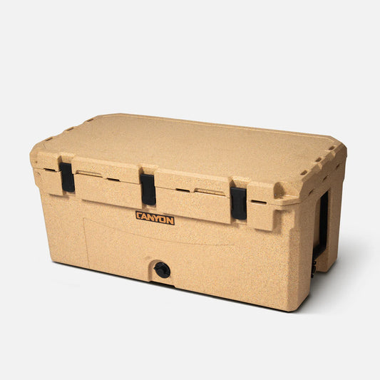 Tan Prospector 125 Raft Cooler from Canyon Coolers with black latches and "Canyon" logo on the front, ideal as an expedition or raft cooler, shown against a plain white background.
