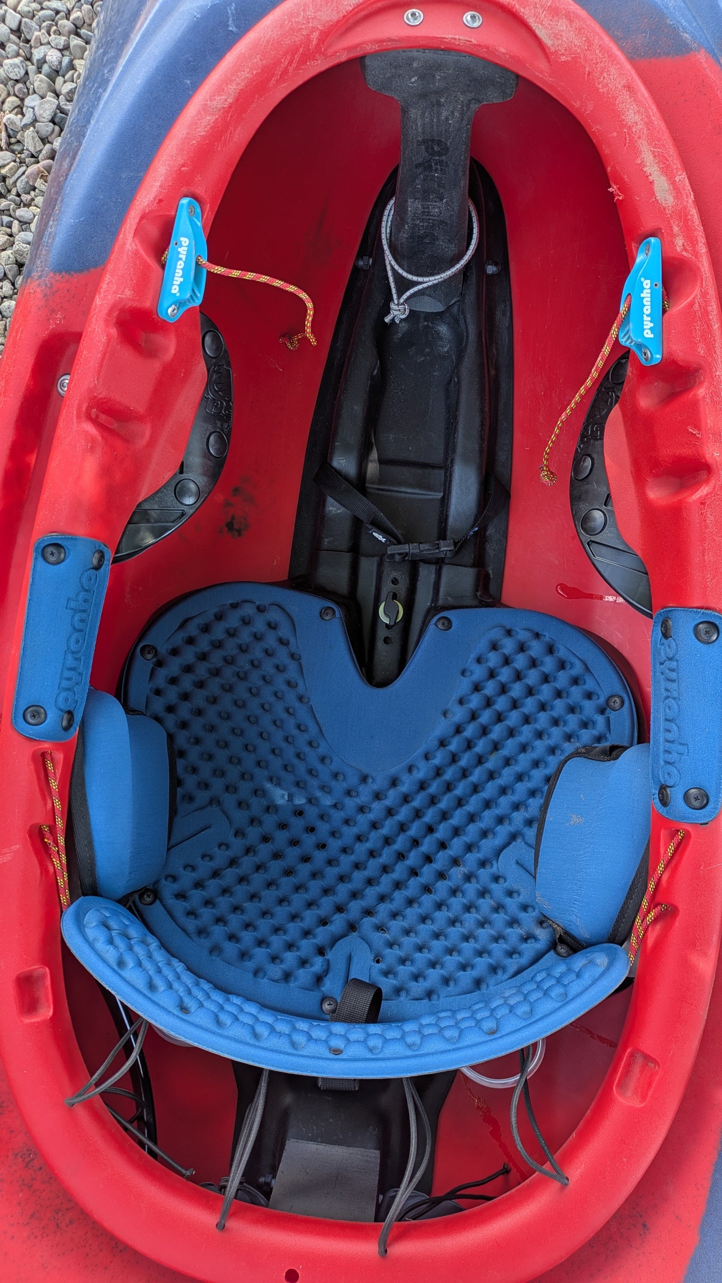 Top-down view of the cockpit of a Pyranha Demo ReactR LG boat in red and blue, featuring a padded blue seat, foot rests, and safety straps.