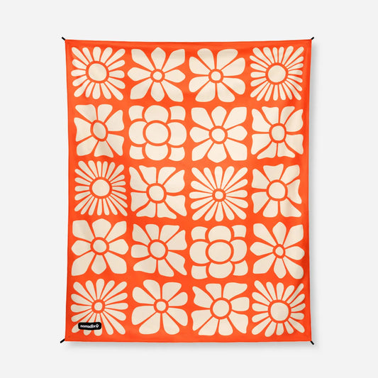 The Nomadix Festival Blanket is orange and features a grid of cream-colored stylized flowers.