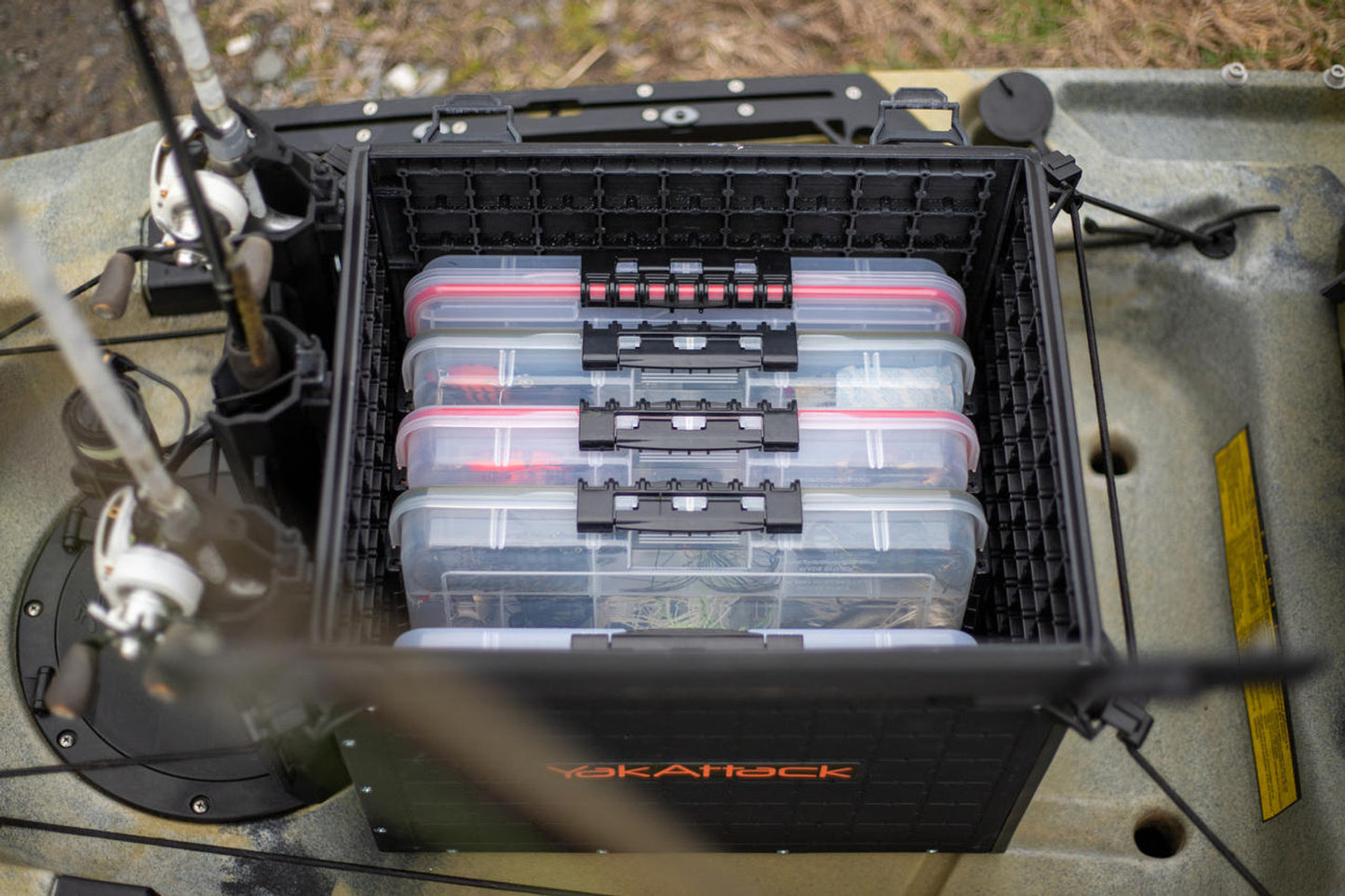 A YakAttack BlackPak Pro Kayak Fishing Crate is on a kayak, neatly organizing four clear tackle boxes with fishing gear between two integrated rod holders.