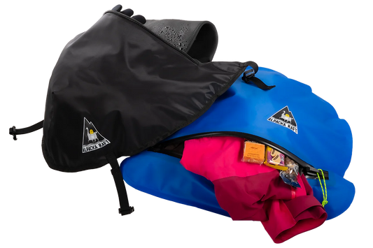 A blue and black Alpacka packraft with a partially open Hybrid Bow Bag zipper, revealing pink fabric and gear inside, perfect for wet storage.