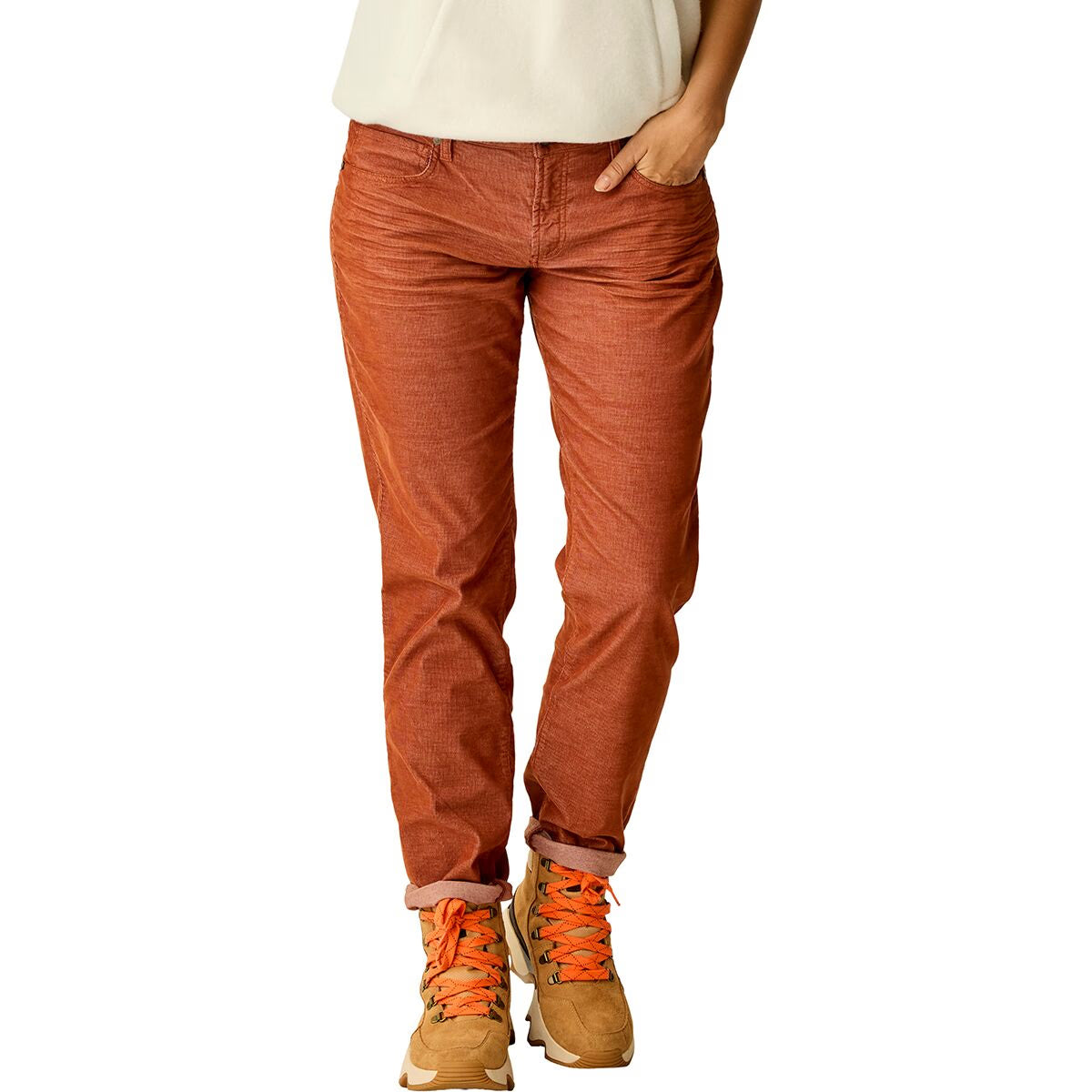 Wearing Carve's Carson Cord rust-colored pants, tan sneakers with orange laces, and a white top, this person stands casually with one hand in their pocket, channeling effortless skater girl style.