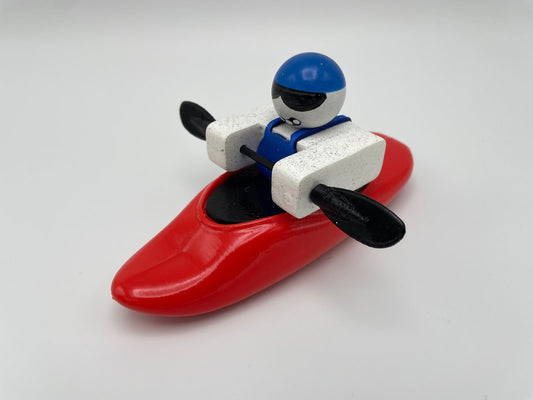 A Foamie Mini Playboat by Foamie Friends features a toy figure in a blue helmet sitting in a red kayak, highlighting an impressive hull design perfect for River Running, all set against a white background.