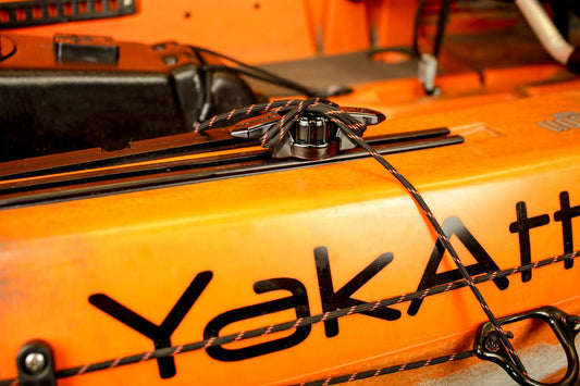 Close-up of an orange kayak with YakAttack branding, featuring the YakAttack GT Cleat Track Mount Line Cleat securing a rope to the side using the kayak's track system.