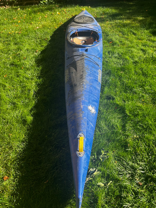 A Pyranha Speeder 14' kayak from 4Corners Riversports stands upright on green grass under bright sunlight, showing dirt marks and a storage hatch near the cockpit—perfect for river running or fast multi-day trips.
