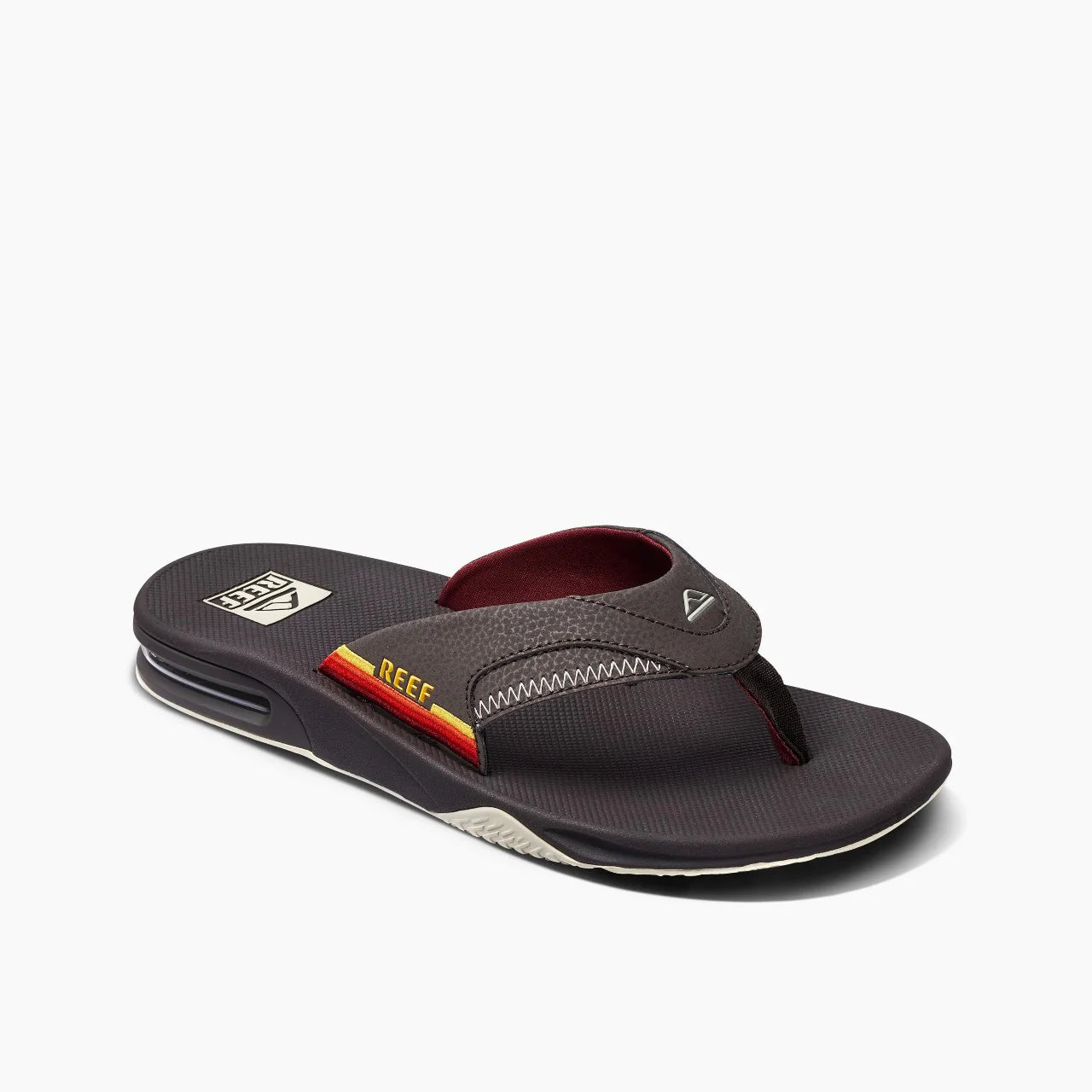 The REEF SANTA ANA flip-flop by REEF features a brown strap with yellow and red stripes, a black sole with visible heel air cushion, and a water-friendly design for versatile wear.