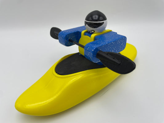 Toy figure in a yellow Foamie Friends plastic play boat with a paddle, wearing a blue jacket and black helmet, isolated on a white background.