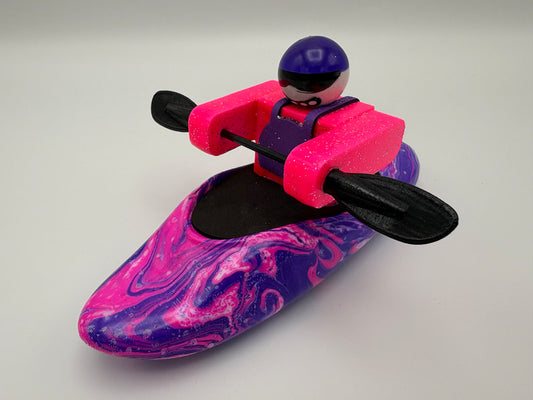 A Foamie Friends Swirl Play Foamie Boaters toy features a figure in a pink and purple marbled boat with a black paddle, wearing a pink vest and purple helmet, set against a plain background.