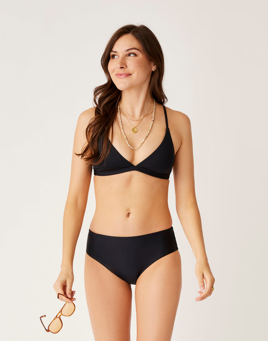 A woman wearing Carve's Pipa Compression Bottom stands against a plain background, looking to the side and holding sunglasses in her left hand.