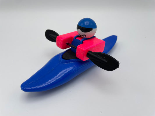 The Foamie Mini Slice by Foamie Friends captures the vibrant charm of Mini Slice boats with its intricately detailed blue kayak and innovative hull design. The figurine, featuring a striking pink life jacket and blue helmet, stands out brilliantly against a white background, epitomizing adventurous performance in miniature form.