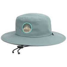 The Heyday Boonie Hat by Outdoor Research is light gray with a wide brim and adjustable chin strap. It features a round logo on the front with an abstract design and text.