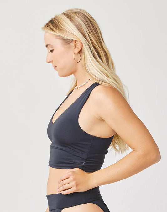Woman with long blonde hair wears the Carve Tofino Top by Carve with matching bottoms, standing in profile against a plain light background.