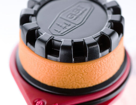 The GSI Outdoors Soft Flask 750ml is displayed with a black cap on a textured orange surface and red base, highlighting its lightweight design for easy portability.