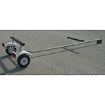 A small boat trailer with a metal frame, two wheels, and a small winch is parked on a paved surface.