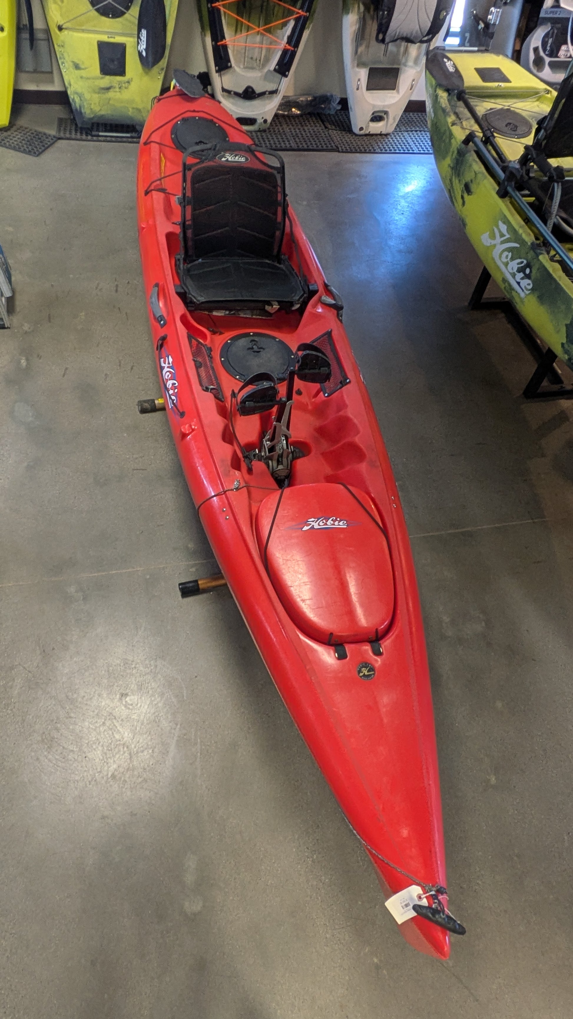A Consignment Hobie Mirage Revolution 13 kayak by 4Corners Riversports, featuring a Vantage CT seat and two storage compartments, is displayed indoors among other kayaks.