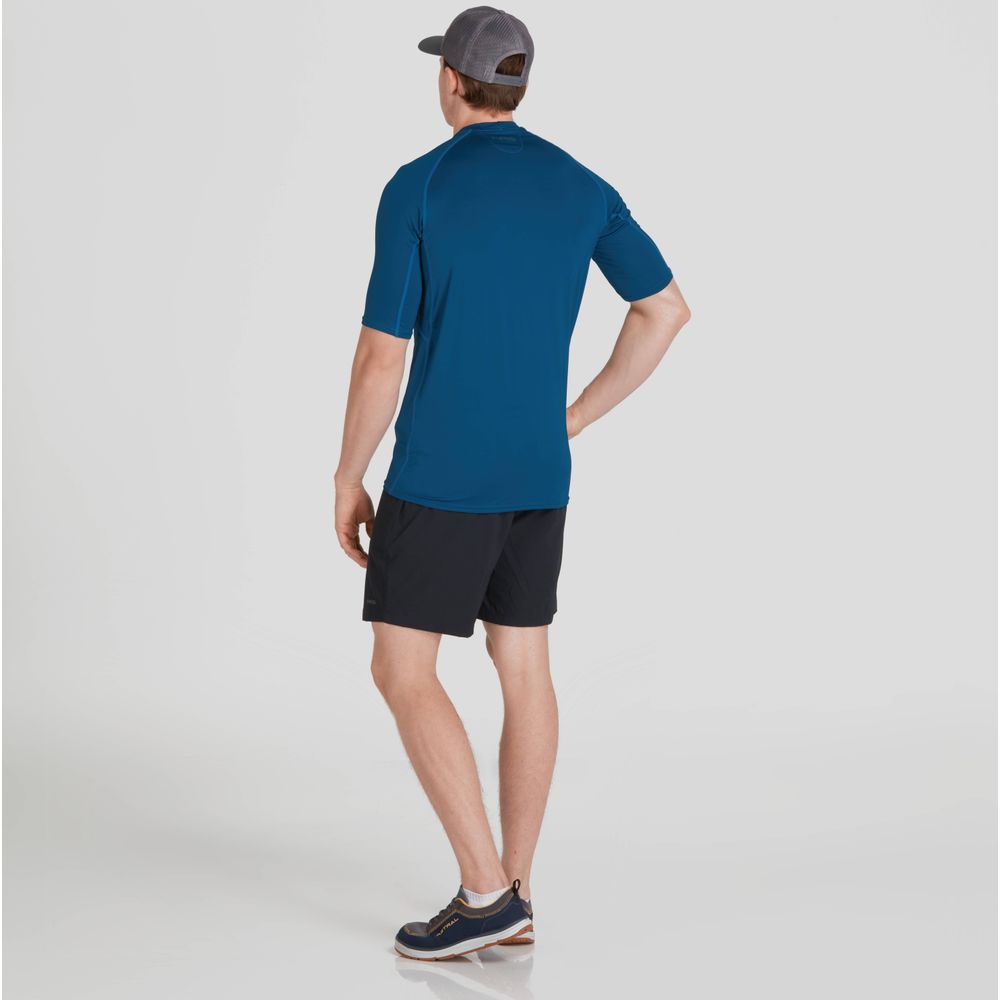 An NRS Short-Sleeve Rashguard-clad man in black shorts and a cap stands facing away in a studio, embodying style and functionality with its moisture-wicking design.