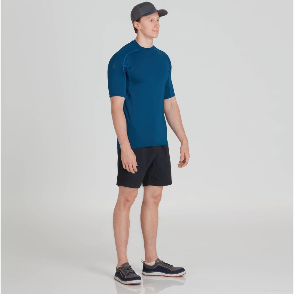 A man in an NRS Short-Sleeve Rashguard, featuring moisture-wicking fabric, paired with black shorts and a gray cap, stands in a neutral pose.