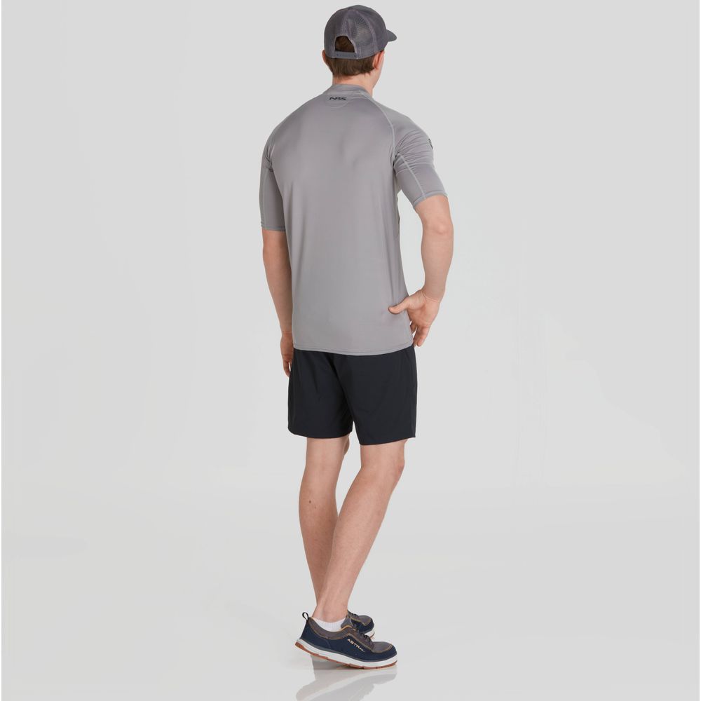 A man in an NRS Men's Short-Sleeve Rashguard, black shorts, and a cap stands with his back to the camera against a plain background, stylishly showcasing sun protection.