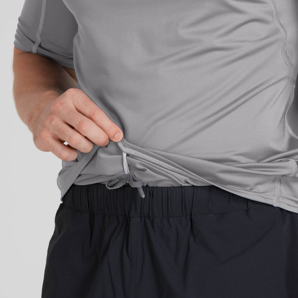 A person in a gray NRS Short-Sleeve Rashguard - Men's and black pants adjusts the shirt's drawstring, ready for sun protection with its moisture-wicking fabric.