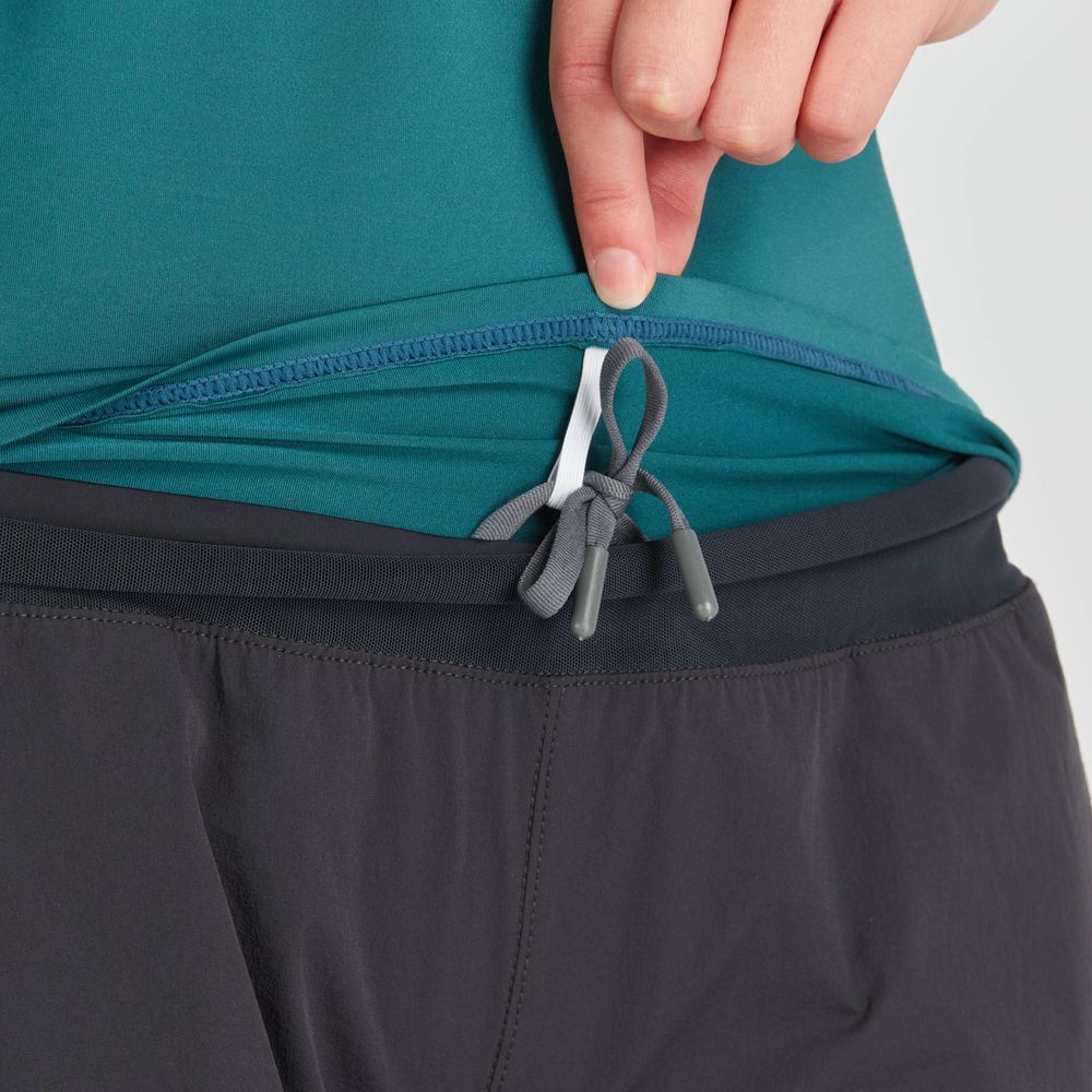 A person adjusts the inner drawstring of black athletic pants, renowned for their moisture-wicking properties, while a turquoise Short Sleeve Rashguard from NRS is partially visible, providing an extra layer of comfort.