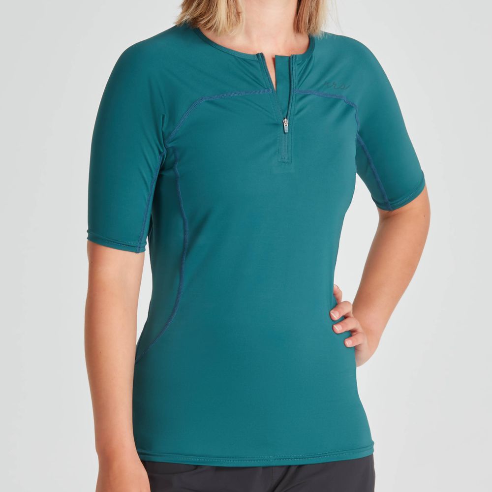 Someone wearing an NRS Short Sleeve Rashguard - Women's in teal stands against a light gray background. The moisture-wicking fabric offers comfort and dryness during any activity.