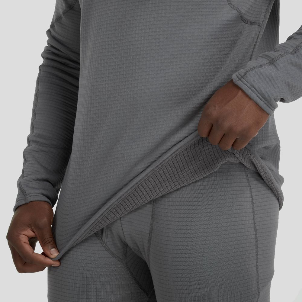 A man wearing an NRS Lightweight Hoodie and pants pulls on the hem of the shirt, which provides sun protection and moisture-wicking comfort in various conditions.
