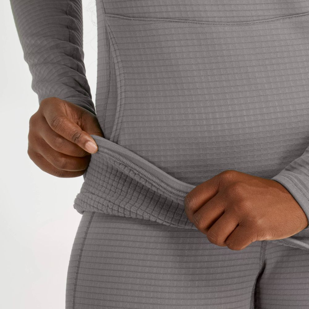 A person is in a gray NRS Lightweight Hoodie for women, crafted from moisture-wicking fabric, along with matching pants, holding the edge of the shirt with both hands.