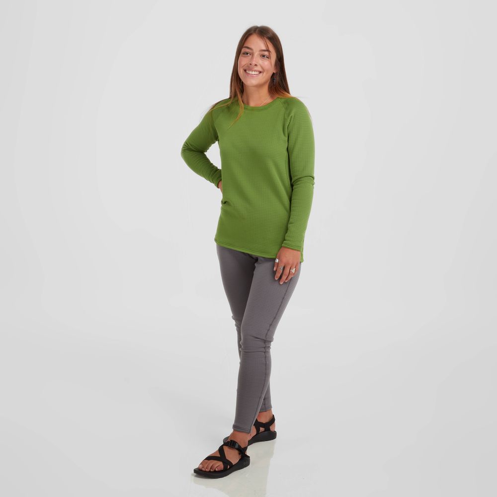 Wearing an NRS Lightweight Shirt - Women's in green and gray pants, a woman smiles with one hand on her hip against a plain white background.