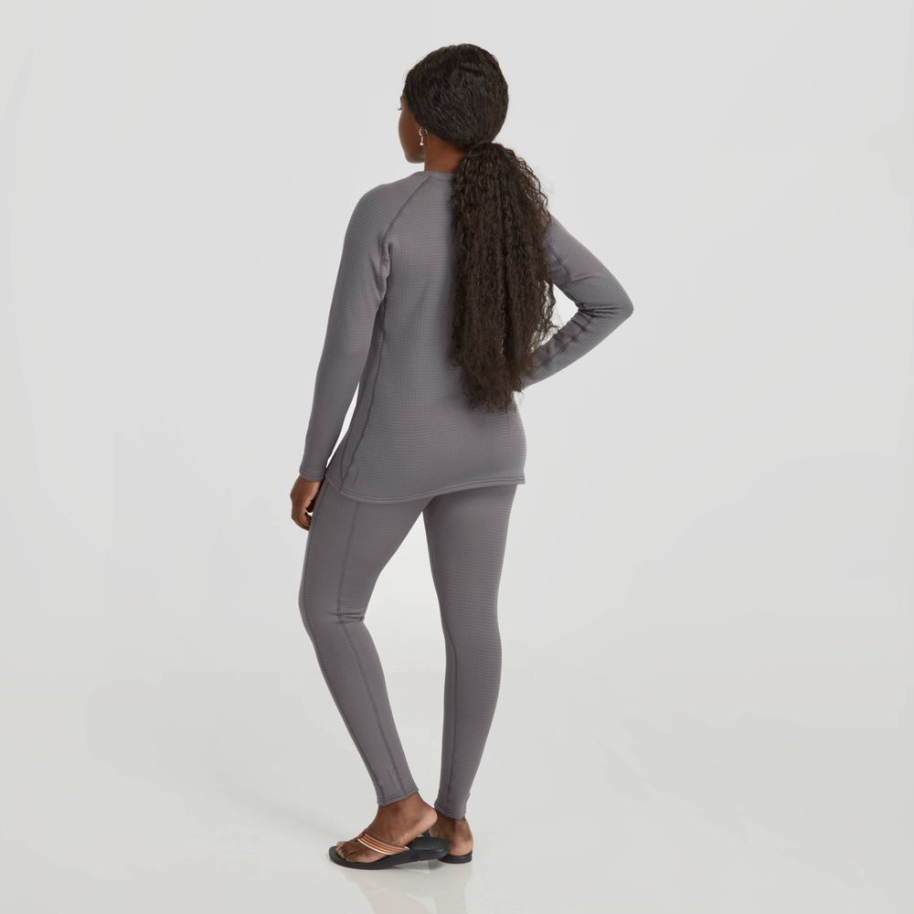 A person stands with long braided hair in a gray NRS Lightweight Shirt - Women's, featuring moisture-wicking properties for comfort during any activity, paired with leggings and facing away with hands near hips.