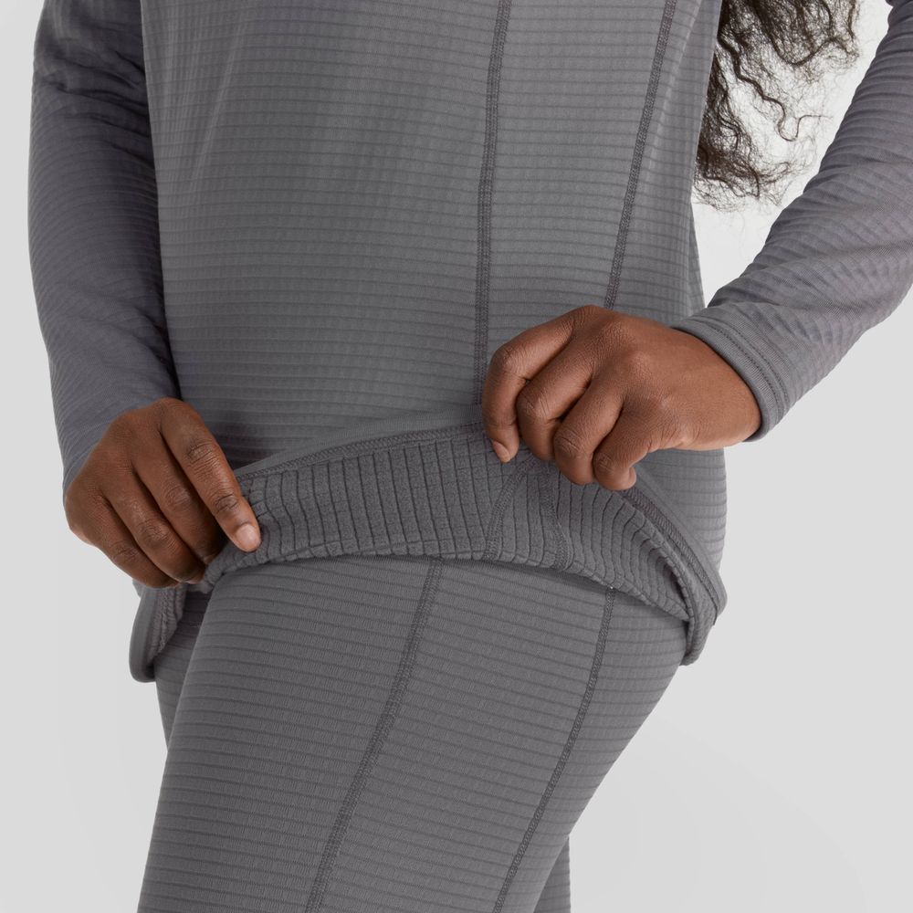 A person adjusts the hem of their NRS Lightweight Shirt - Women's, a textured, gray long-sleeve top and bottom set that offers moisture-wicking comfort.