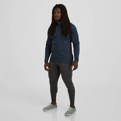 A person with long hair stands against a plain background, wearing a navy NRS Expedition Weight Shirt - Men's with UPF 50+ protection, gray leggings, and light gray shoes.