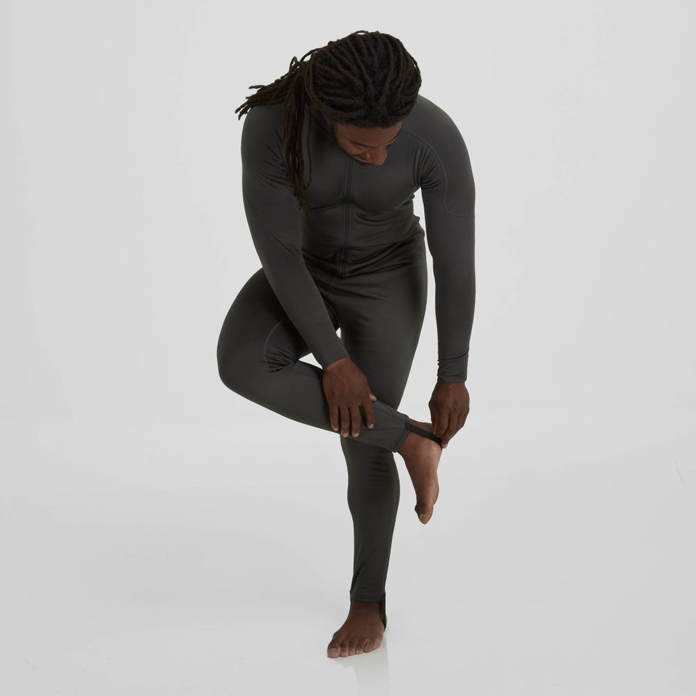 An individual bends forward in a fitted, long-sleeve black Expedition Weight Union Suit by NRS, adjusting the recycled material pant leg. The plain white background highlights the sleek silhouette and eco-friendly design.