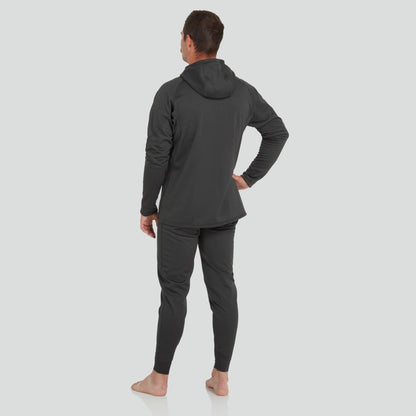 A barefoot individual in a dark NRS Expedition Hoodie for men and high-stretch joggers is seen from behind, facing away with one hand on their hip against a light backdrop.