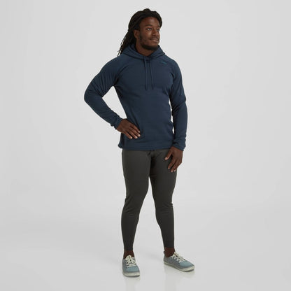 A man in an NRS Expedition Hoodie, made from breathable fleece, stands with hands on hips against a plain background, wearing gray leggings and sneakers.