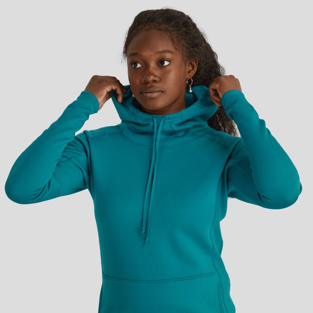 A woman wearing an NRS Expedition Hoodie adjusts the neck with both hands against a plain gray background, enjoying the breathable insulation of its high-stretch fleece.