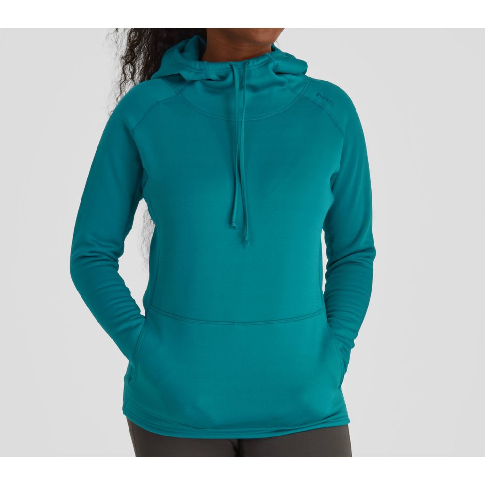 A woman stands against a plain backdrop, wearing an NRS Expedition Hoodie with breathable insulation and a front pocket in teal, paired with black pants.