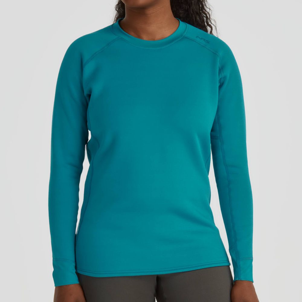 The person stands against a plain background, wearing the NRS Expedition Fleece - Women's, a teal long-sleeve shirt made from recycled material, paired with dark pants.