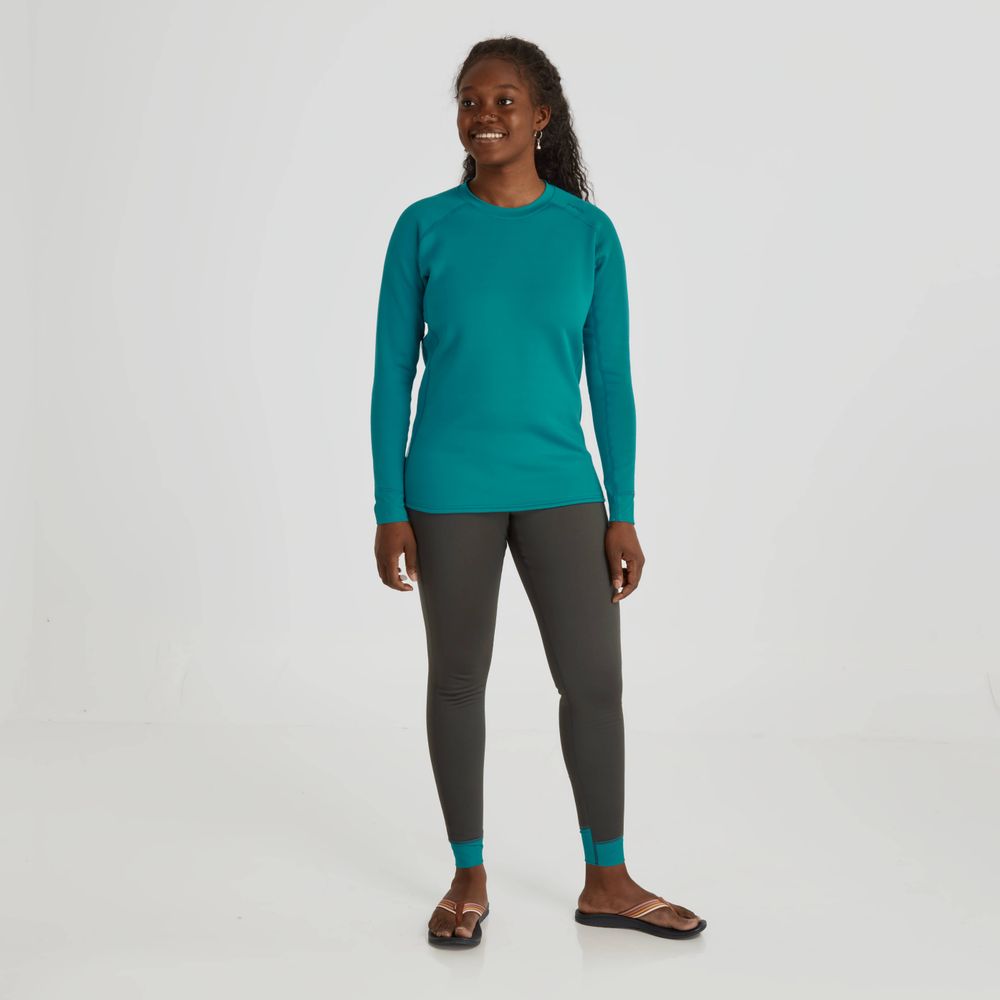 A person in a teal long-sleeve shirt, NRS Expedition Weight Pants for women with teal cuffs and a high-rise waist, and brown sandals smiles against a white background.